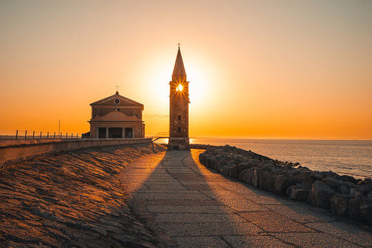 Sunrise Over Church Tower in Caorle, Italy

Magical sunrise at the Adriatic coast in Caorle, Italy, with the rising sun forming a perfect star through the church tower. A peaceful coastal scene.
