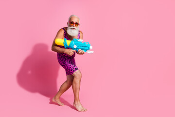 Photo of glamour senior man play watergun beach game wear leopard print swimsuit isolated pink...