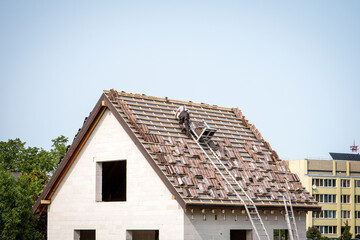 Worker Installing Roof Tiles on House Under Construction with Ladder and Safety Equipment
