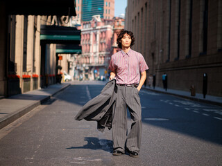 Portrait of handsome Chinese young man wearing gray suit posing in the street, young guy with black curly hair with urban background. Male fashion, cool Asian young man lifestyle.