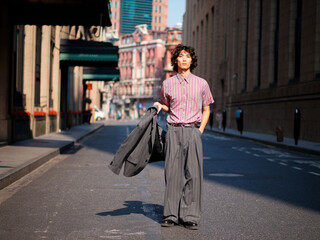 Portrait of handsome Chinese young man wearing gray suit posing in the street, young guy with black curly hair with urban background. Male fashion, cool Asian young man lifestyle.