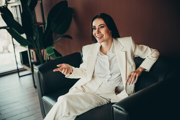 Beautiful businesswoman in formal white attire gesturing while seated in a stylish office setting...