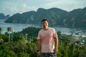 A guy in a pink wet T-shirt stands against the backdrop of the island of Pi Pi Don