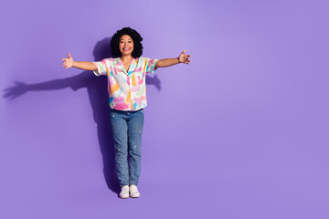Young cheerful woman in vibrant casual fashion posing with open arms on a bright violet background conveying joy and positivity