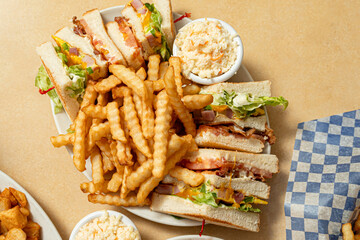 classic club sandwich platter featuring layers of toasted white bread filled with ham, cheese, crispy bacon, lettuce, tomato, and mayonnaise. crinkle-cut French fries and a side of creamy coleslaw,