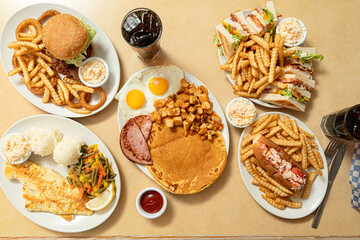 cheeseburger with fries and onion rings, pancakes with eggs, potatoes, ham, a fish fillet with mashed potatoes and mixed vegetables, a lobster roll with fries, and a club sandwich served with coleslaw