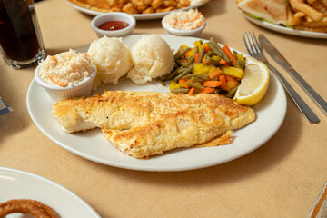 pan-fried white fish fillet served with a wedge of lemon, two scoops of mashed potatoes, mixed steamed vegetables (green beans, carrots, and bell peppers), and a side of creamy coleslaw.