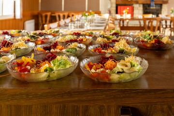 Closeup on salad bowls in the foreground, with set table tables in the background. Selective focus.