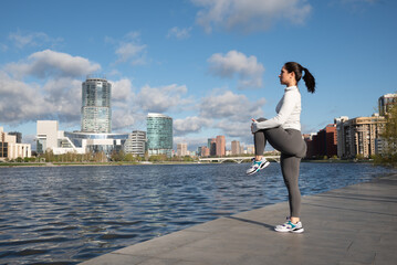 Sporty Woman Stretching Outdoors by the City Waterfront at Sunrise