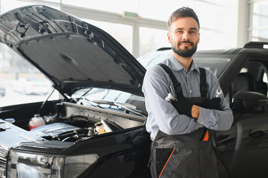 Friendly mechanic in modern car repair shop with car. Professional technician checking vehicle diagnostics and maintenance. Concept of automotive industry and customer service