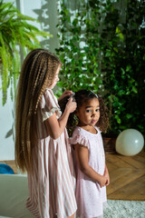 A little girl is gently combing the beautiful hair of another little african american girl