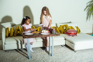 Two little girls are at a table set for a birthday party