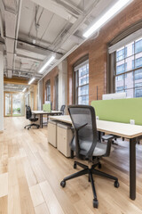 A spacious contemporary open-concept coworking space featuring wooden floors, large windows, and modern desks arranged in a collaborative layout