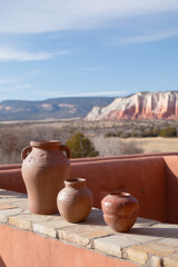 Elegant adobe pottery sits on a rustic terrace overlooking a scenic desert landscape with colorful cliffs in the background under a clear blue sky