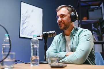Man podcaster influencer blogger smiling while broadcasting his live audio podcast in studio using...