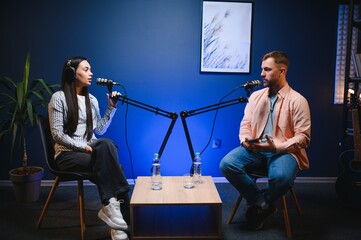 Female podcaster in headphones interviewing man guest using microphone, smiling, recording and...