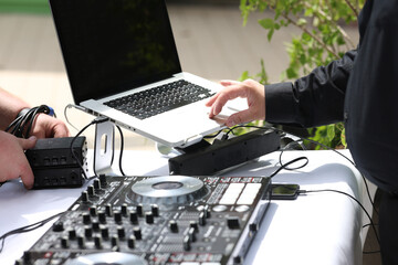Close-up of DJ mixing setup with laptop and audio controller during outdoor event. Hands adjusting...