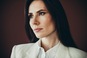 Professional businesswoman in formal white attire gazing with confidence against a subtle background
