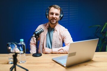 Man podcaster influencer blogger smiling while broadcasting his live audio podcast in studio using...