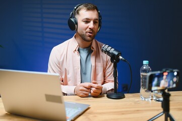 Man podcaster influencer blogger smiling while broadcasting his live audio podcast in studio using...