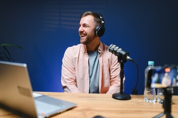 Man podcaster influencer blogger smiling while broadcasting his live audio podcast in studio using...