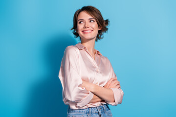 Young woman in satin pink blouse with charming smile against blue background, expressing happy...