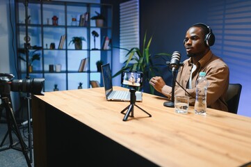 Young african american male vlogger recording video blog in studio with professional microphone.