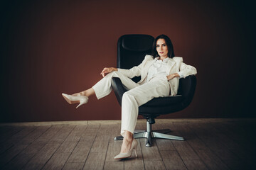 Professional businesswoman in elegant white suit seated confidently in a modern office chair...