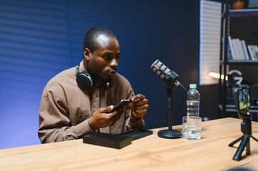 Black vlogger filming podcast on smartphone in studio. Cheerful blogger