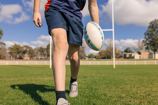 Waist-down view of junior rugby union player holding ball on field in front of goal posts