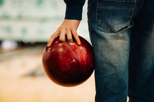 Close up of teenage boy's hand with fingers in holes of red bowling ball