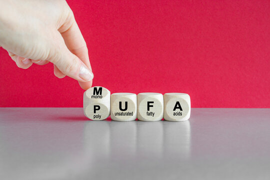 Hand turns cube and form the acronym MUFA (Monounsaturated Fatty Acids) and PUFA (Polyunsaturated Fatty Acids). Beautiful red background. Business and medical concept.