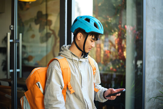 Asian delivery guy walking out of the restaurant while on his phone.