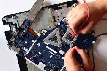 young man who is a computer technician A laptop motherboard repairman is using an IC meter to look for defects on the motherboard to repair on his desk. Board repair with modern technology