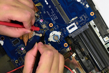 young man who is a computer technician A laptop motherboard repairman is using an IC meter to look for defects on the motherboard to repair on his desk. Board repair with modern technology