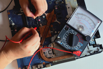 young man who is a computer technician A laptop motherboard repairman is using an IC meter to look for defects on the motherboard to repair on his desk. Board repair with modern technology