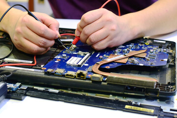 young man who is a computer technician A laptop motherboard repairman is using an IC meter to look for defects on the motherboard to repair on his desk. Board repair with modern technology