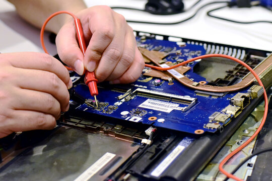young man who is a computer technician A laptop motherboard repairman is using an IC meter to look for defects on the motherboard to repair on his desk. Board repair with modern technology