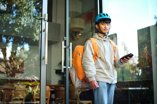 Asian delivery guy walking out of the restaurant while on his phone