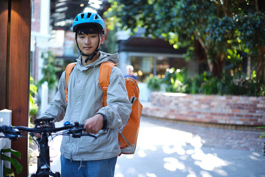 Asian delivery boy walking with his bicycle.
