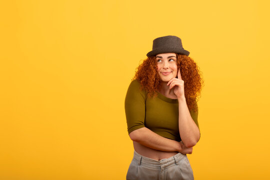 Pensive redhead woman planning with hand on chin, yellow background