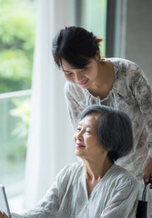 Asian family moment cheerful daughter helping elderly mother both smiling indoors natural light warm relationship caregiving happiness togetherness support