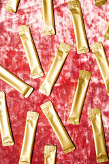 Gold Cosmetic Sachet Randomly Scattered on Red Velvet Background. Beauty Product Packaging Design with Luxury Concept.