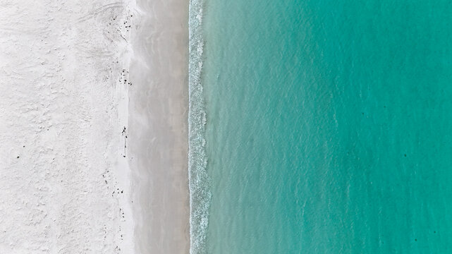 Aerial of clear blue water meeting white sand