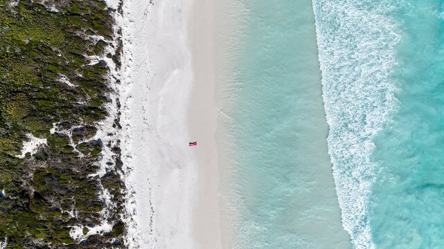 Aerial of person laying on pink towel on beach with crystal blue water