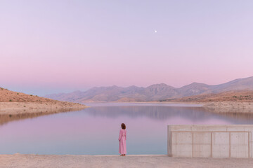 Fototapeta premium minimalist scene featuring person in pink clothing standing before hydroelectric dam in turkey at sunset