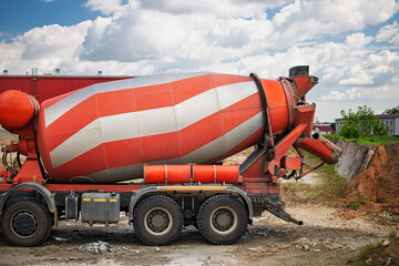 Concrete mixer truck operates on construction site under blue sky with white clouds during daytime