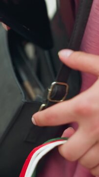 Hand view of lady searching through her handbag to retrieve her phone, followed by taking out a lemon-colored card, with a partial view of her shopping bag in her hand with a blurred surrounding