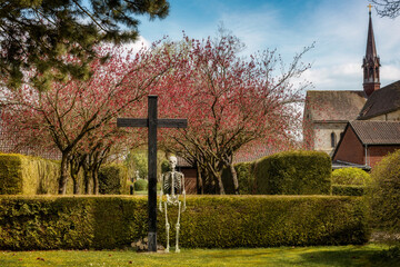 Blick vom Friedhof auf das Kreuz neben dem ein Skelett steht im Hintergrund die Klosterkirche Loccum
