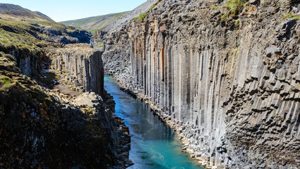 Breathtaking views of Studlagil Canyon showcase towering basalt columns alongside a vibrant blue...